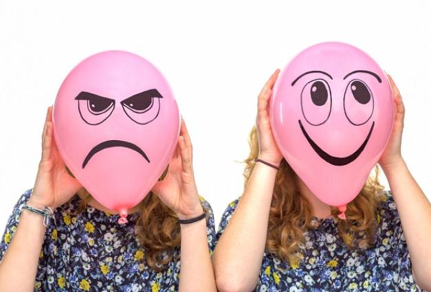Image of a lady holding two balloons with a happy and sad face in front of her own face
