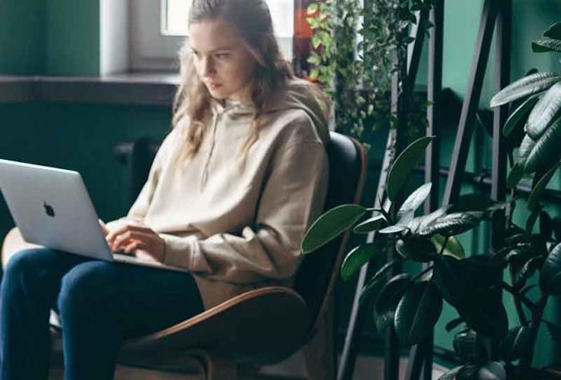 Young woman working on laptop surrounded by plants