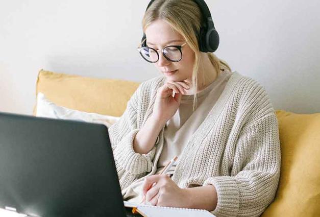 Young woman sitting on sofa studying with laptop and headphones