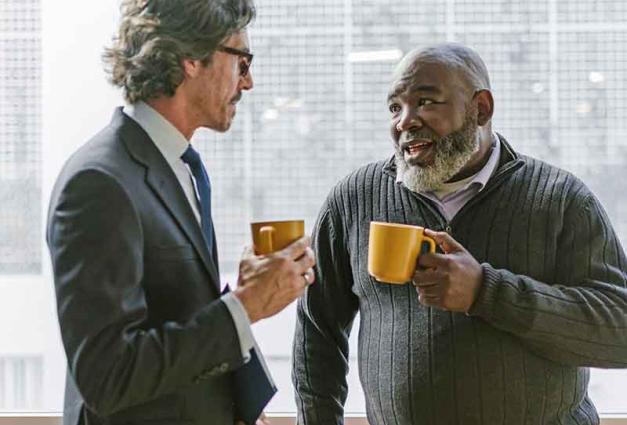 Two men drinking coffee and having conversation near window