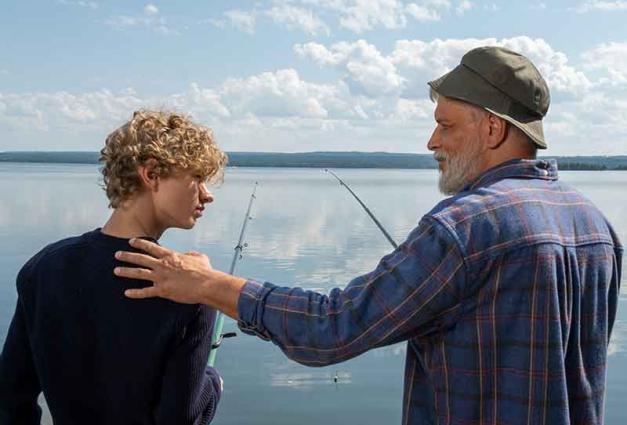 Older man touching teenage boy on shoulder near water while fishing