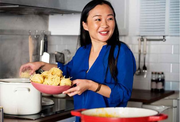 Asian woman cooking noodles in her kitchen
