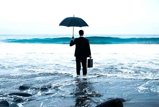 businessman standing on beach holding an umbrella