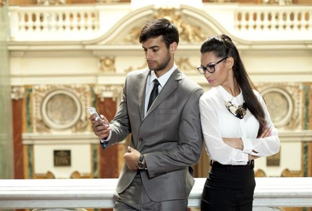 Image of a young businessman looking at his phone with a young businesswoman looking over his shoulder