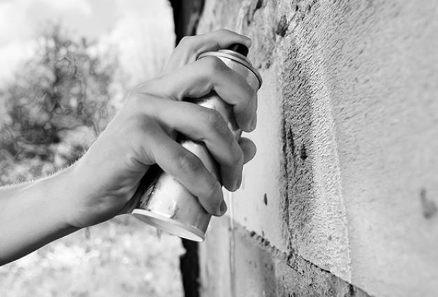 Image of hand holding a spray paint can near a wall