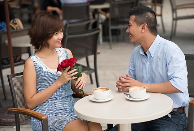 Image of couple sitting at small table, woman is holding flowers
