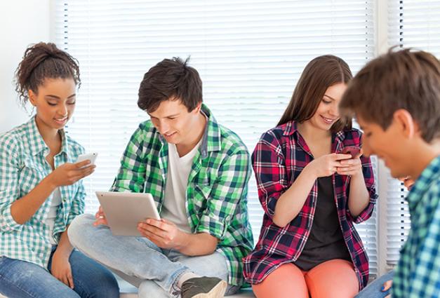Image of four young boys and girls sitting near one another, all using tablets or phones