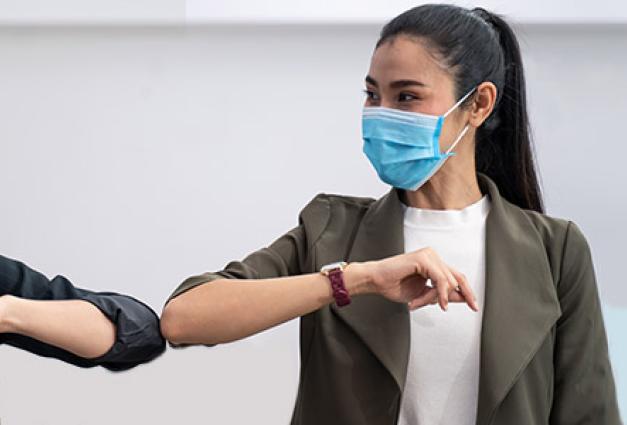 Two young women wearing face masks bump elbows