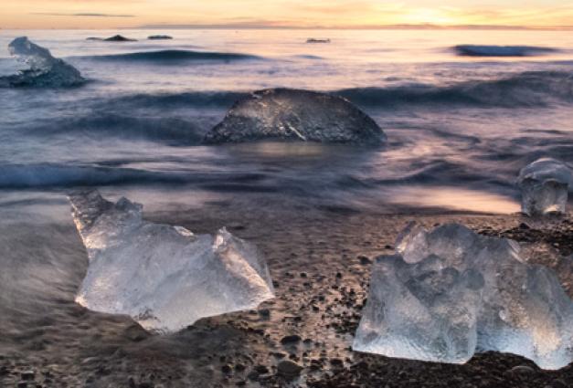 Image of blocks of ice resting on a calm beach as the sun sets