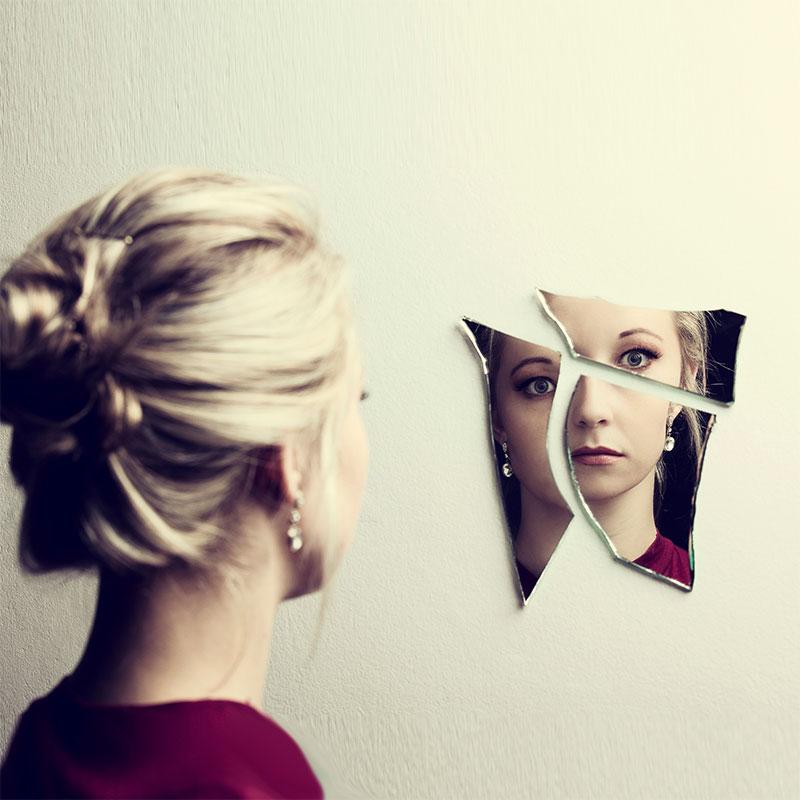 Woman looking at her face in three shards of broken mirror