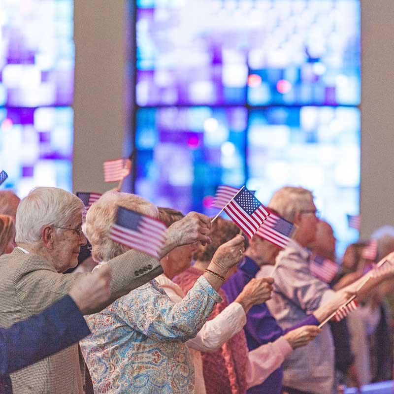 Senior parishoners holding small U.S. flags in a church