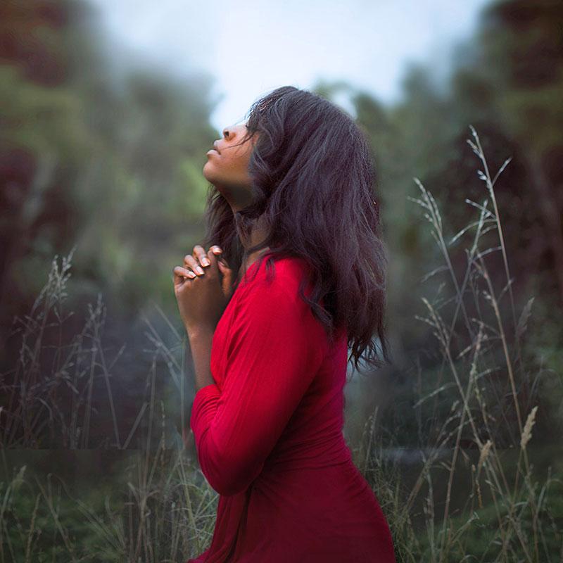Young Black woman standing in a field looking to the sky and praying  