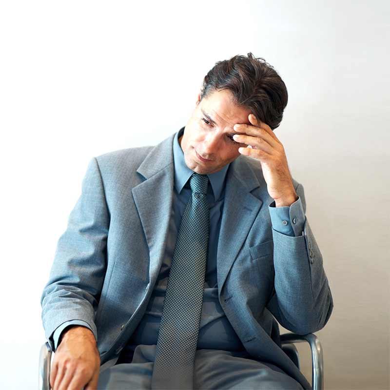 Dejected professional man sitting and holding his forehead in his hand 
