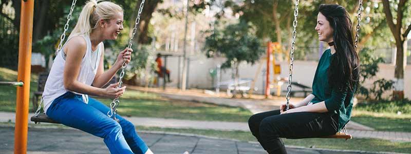 Two young women sitting on swings chatting