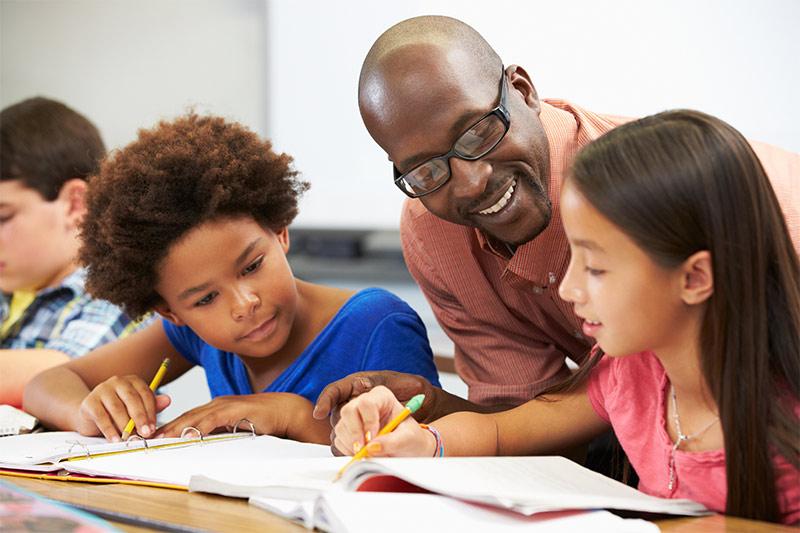 Image of teacher working with young students on schoolwork
