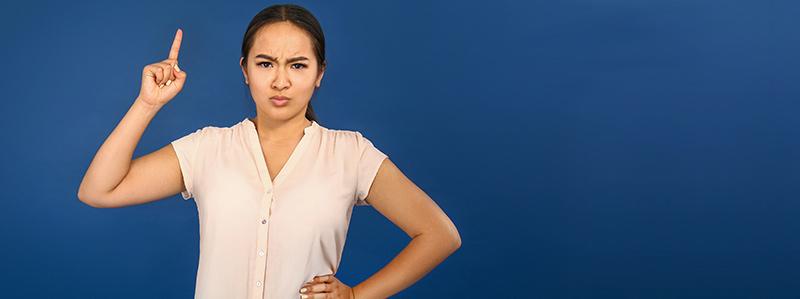 angry Asian woman with raised index finger on color background