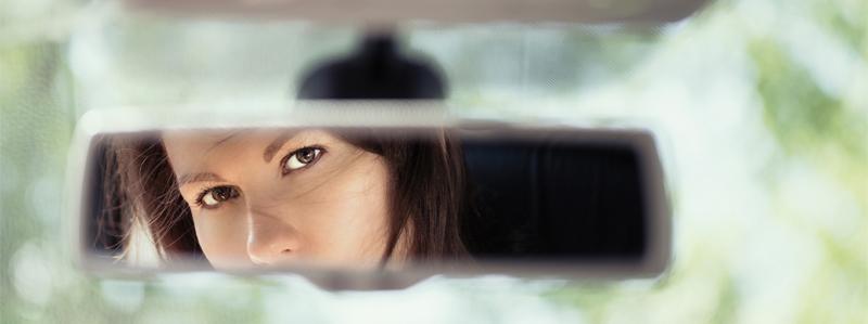 Reflection of a young woman's face in a car's rear view mirror.