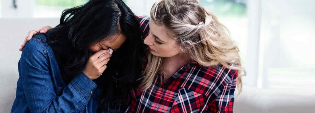 Young woman consoling crying female friend at home